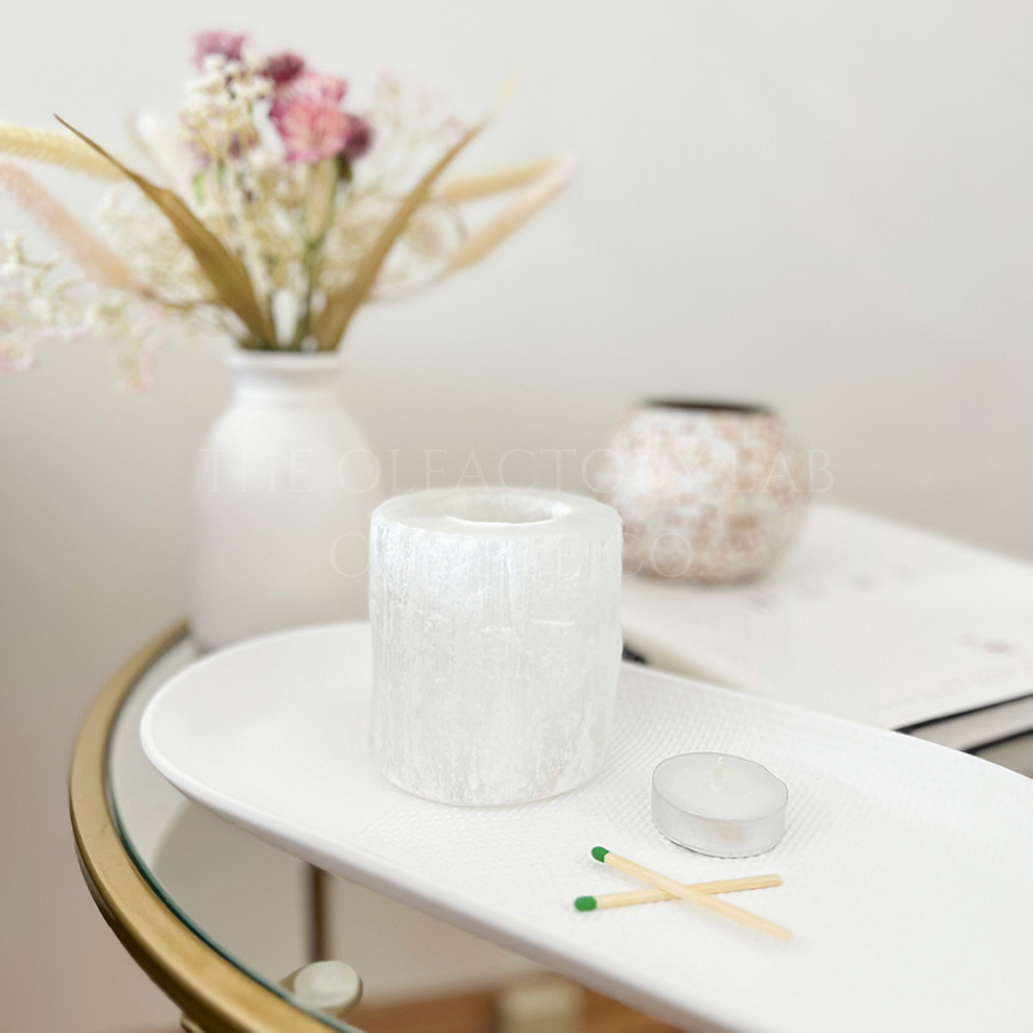 
                  
                    Selenite holder on a white tray with a tea light and set of matches beside it to demonstrate the tea light holders purpose. In the background is a white hardcover book, and pink dried florals.
                  
                
