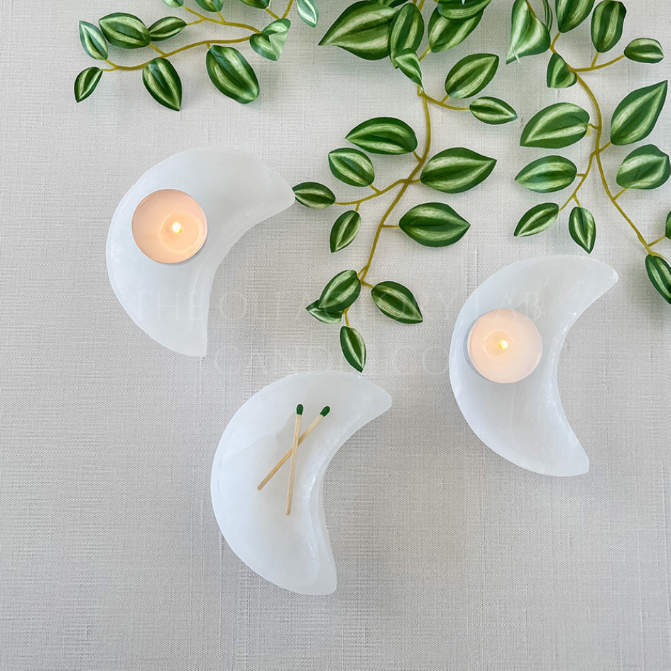 
                  
                    Three selenite moon bowls shown from a birdseye view near some vines. Inside the moon bowls are two tea lights and a pair of matches.
                  
                