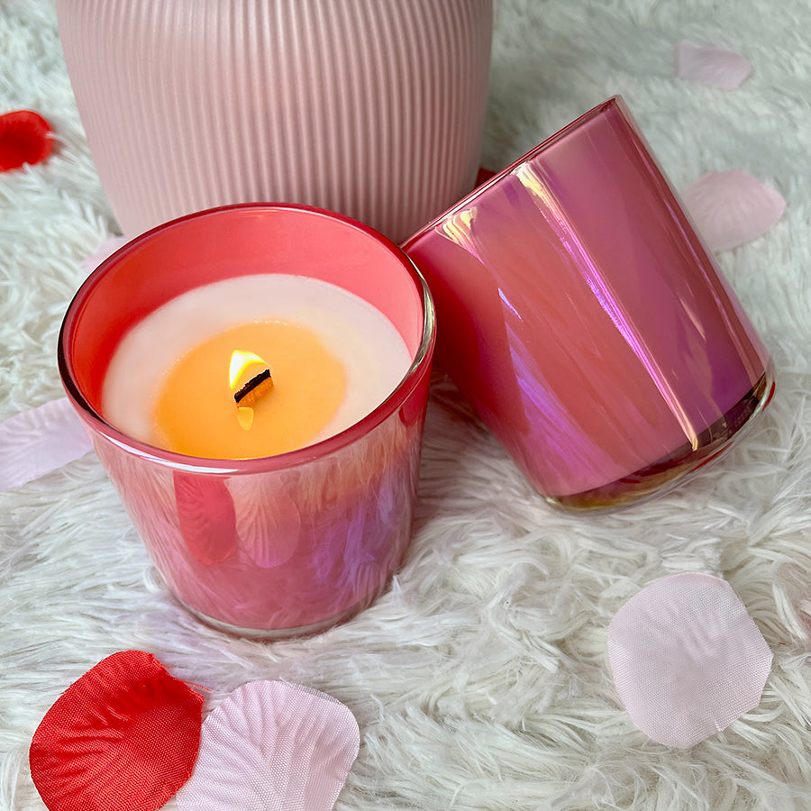 
                  
                    13oz iridescent pink candle with a lit wood wick. Candle is sitting on a white faux fur carpet surrounded by pink and red rose petals. 
                  
                
