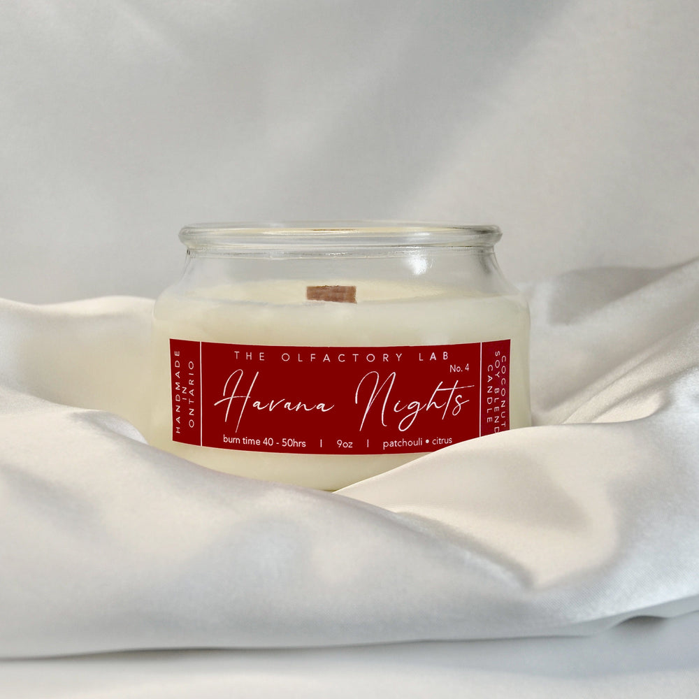 9oz Havana Nights candle. Label is a rectangle in a true red colour with white cursive font. The candle is sitting on white silk with a white background. 