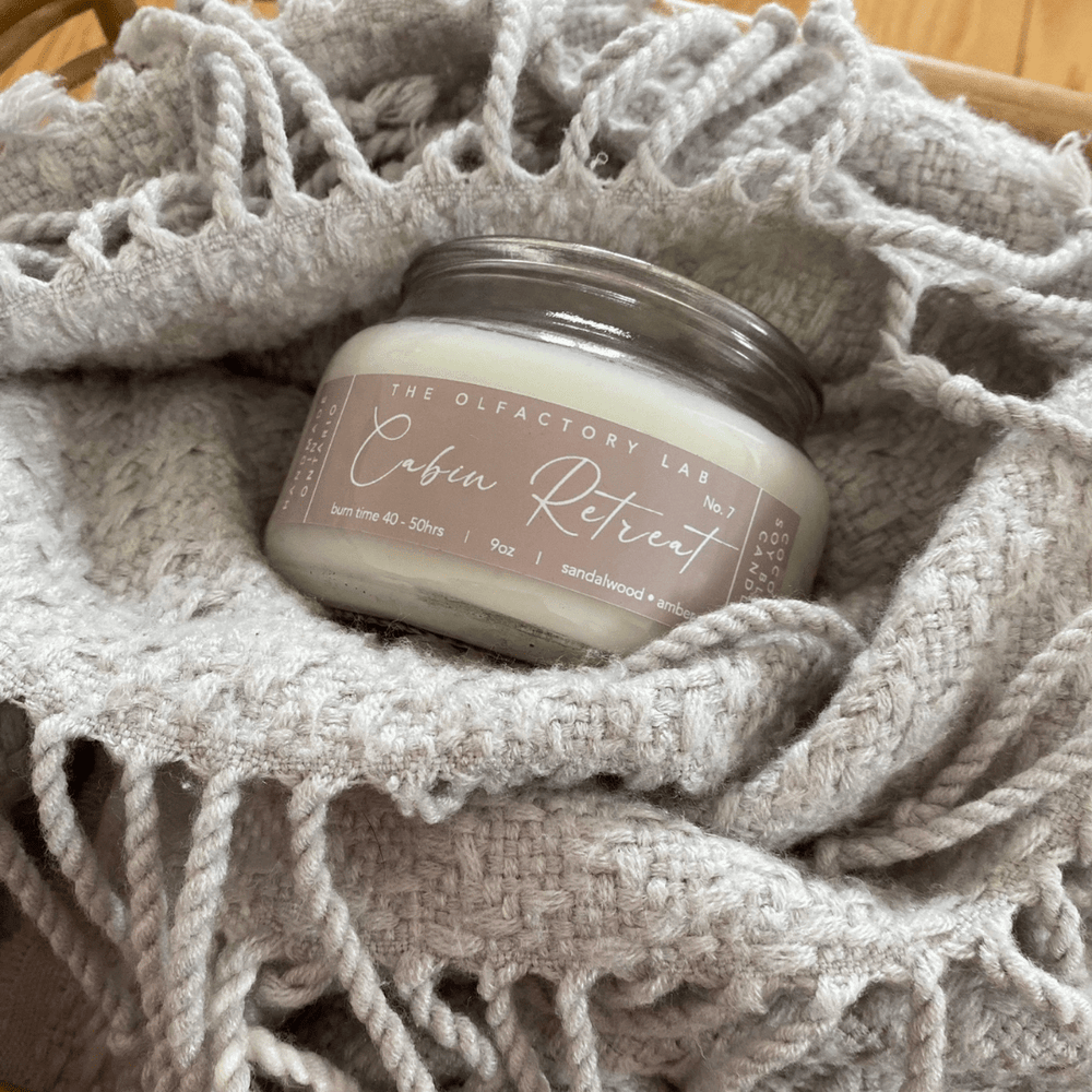 Cabin Retreat nine ounce candle sitting in a grey knitted blanket.