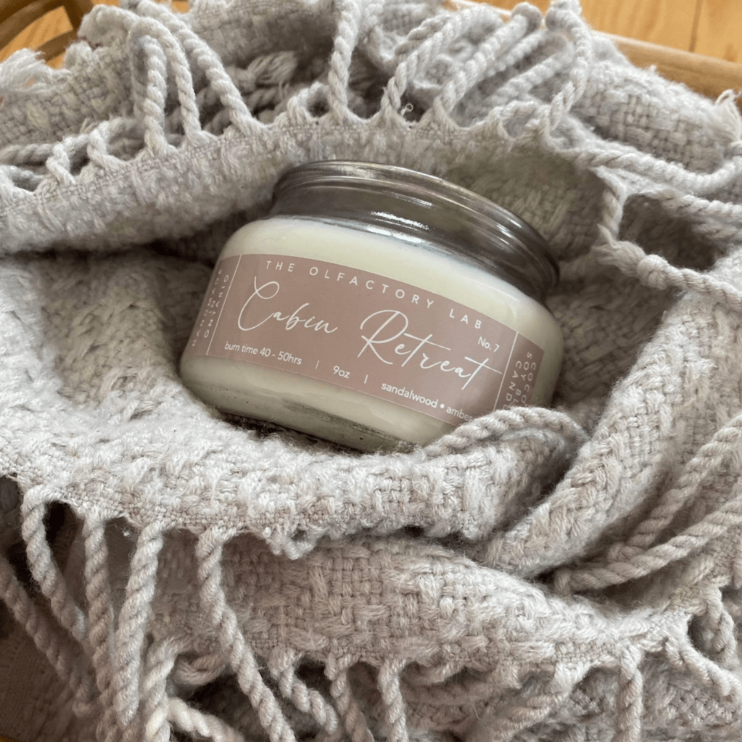 
                  
                    Cabin Retreat nine ounce candle sitting in a grey knitted blanket.
                  
                