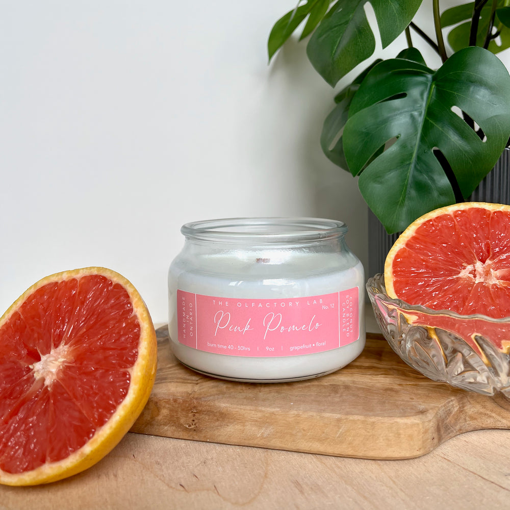 
                  
                    9oz white candle. Candle is sitting on a wood cutting board in the middle of two fresh grapefruits. The candle label is a rectangle shape in a soft pink colour, with white cursive font reading Pink Pomelo. 
                  
                