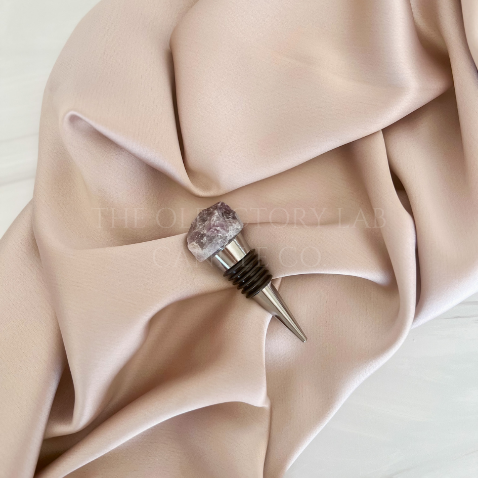 
                  
                    Silver wine stopper with a Amethyst crystal top. The wine stopper is displayed in the middle of a soft pink silk background.
                  
                
