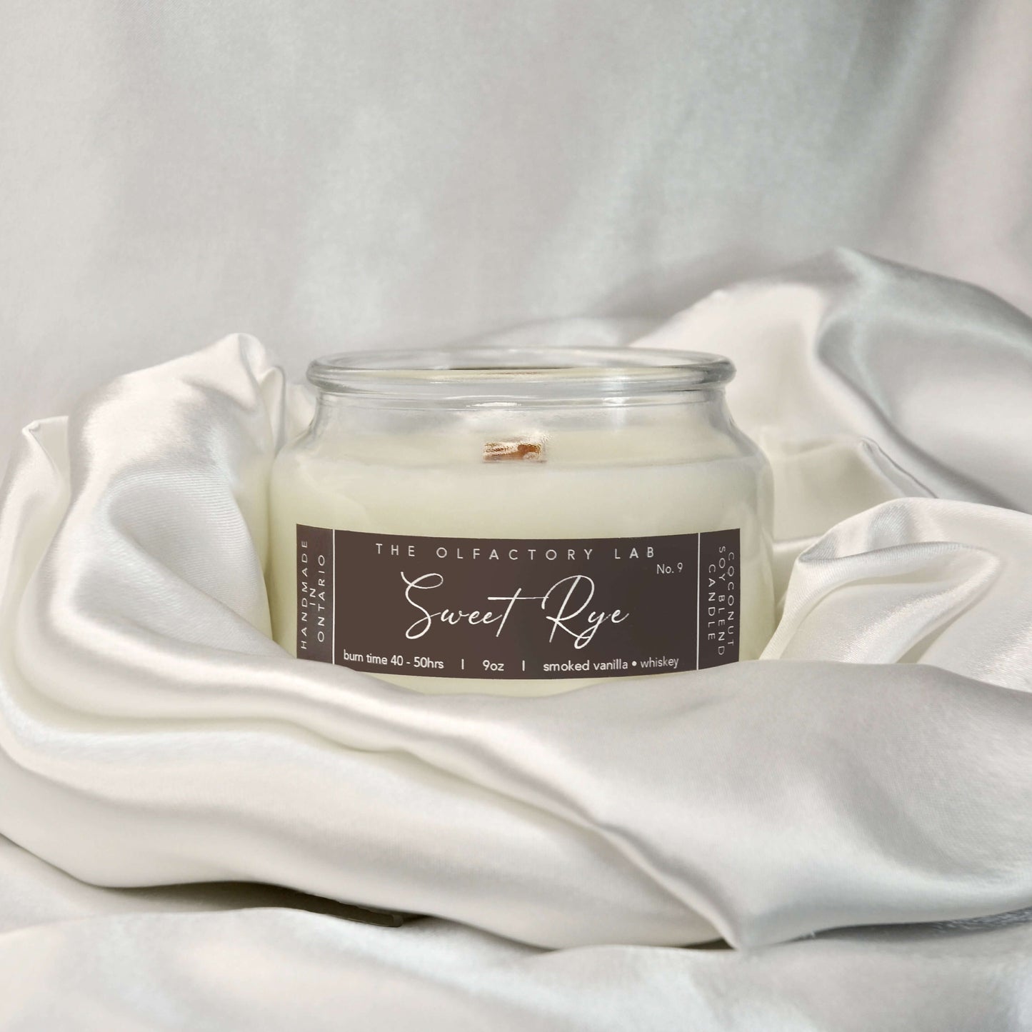 
                  
                    9oz white candle. Candle label is a rectangle shape in a dark brown colour with white cursive font reading Sweet Rye. Candle is placed in the centre of a white silk pillow. 
                  
                
