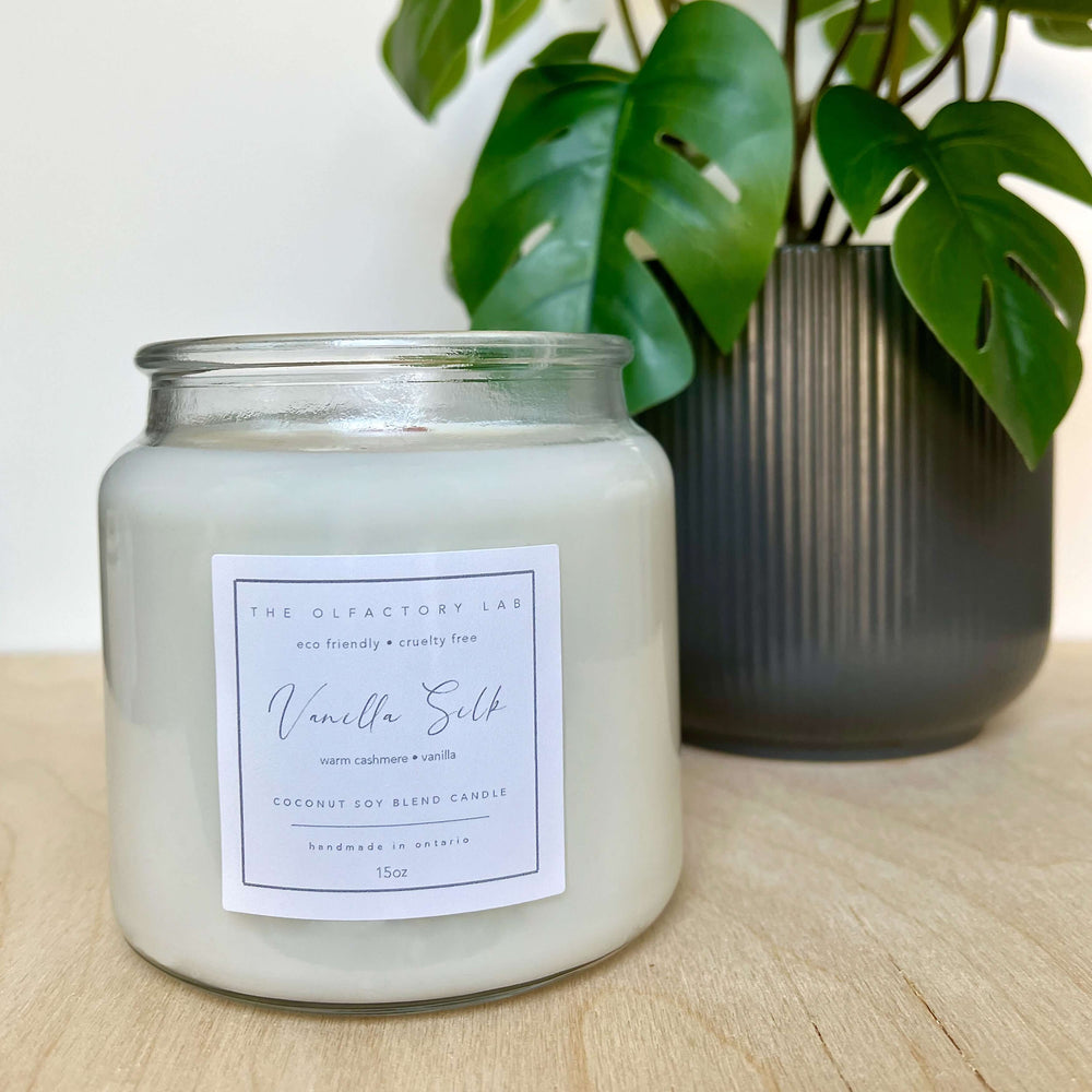 
                  
                    15oz white candle. The candle label is a square shape in a soft yellow colour with grey cursive font reading Vanilla Silk. The candle is displayed on a wood table with greenery in the background.
                  
                