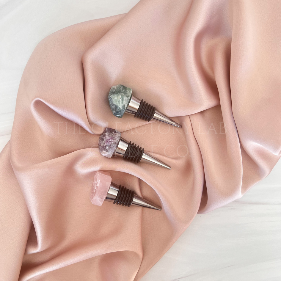 
                  
                    3 silver wine stoppers placed in the middle of a soft pink silk background. The wine stoppers are topped with Rose Quartz, Amethyst, and Fluorite crystals. The photo is to demonstrate a bundle deal purchase option that includes all 3 crystal wine stoppers for less.
                  
                