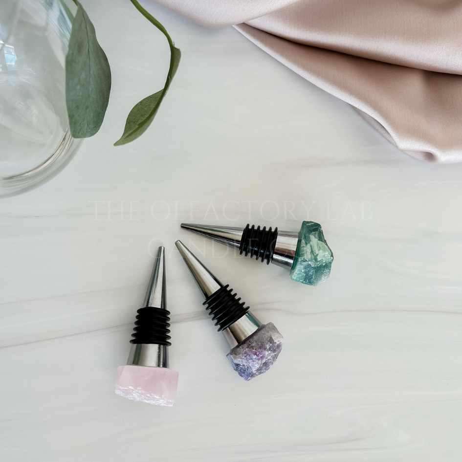 
                  
                    3 crystal wine stoppers on a grey marble surface. The wine stoppers are silver with a crystal top in Rose Quartz (soft pink), Amethyst (purple), and Fluorite (green/purple).  
                  
                